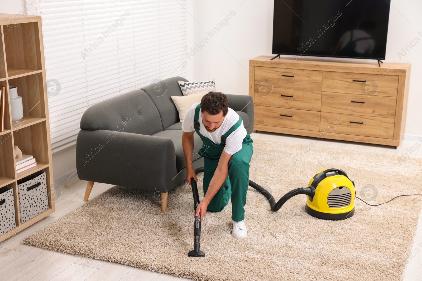 Photo of Dry cleaner's employee hoovering carpet with vacuum cleaner in room