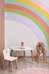 Photo of Cute children room interior with stylish furniture, toy bunny and rainbow art on wall