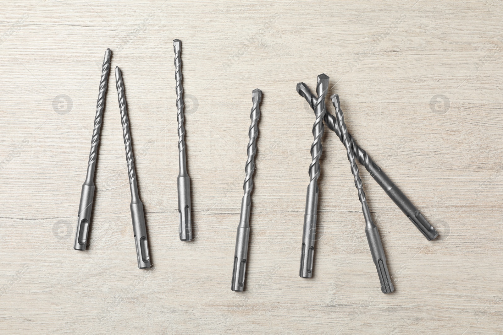 Photo of Different drill bits on white wooden table, flat lay