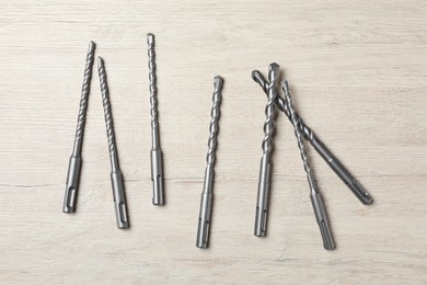 Different drill bits on white wooden table, flat lay