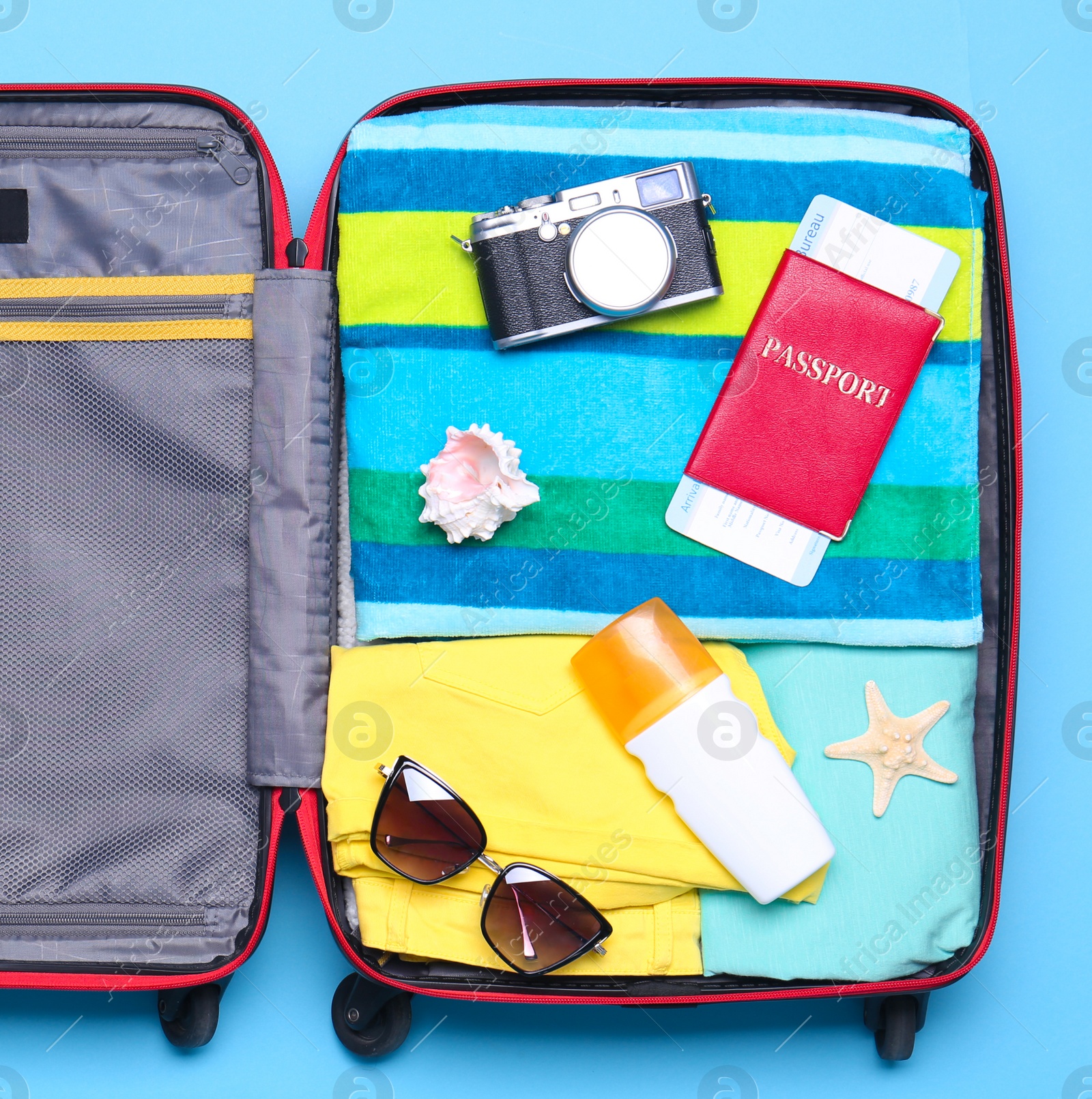 Photo of Open suitcase with beach objects on blue background, top view