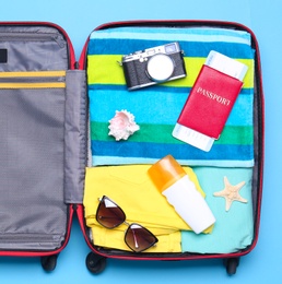 Photo of Open suitcase with beach objects on blue background, top view