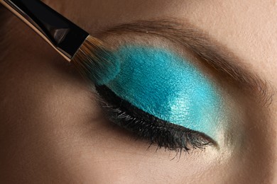 Photo of Applying cyan eye shadow onto woman's face, closeup. Beautiful evening makeup