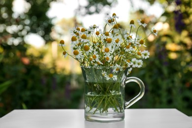 Photo of Beautiful bouquet of chamomiles in glass cup on white table outdoors