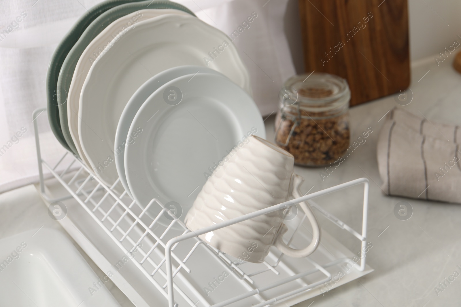 Photo of Drainer with different clean dishware and cup on light table indoors