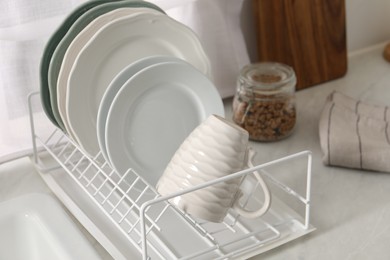 Drainer with different clean dishware and cup on light table indoors