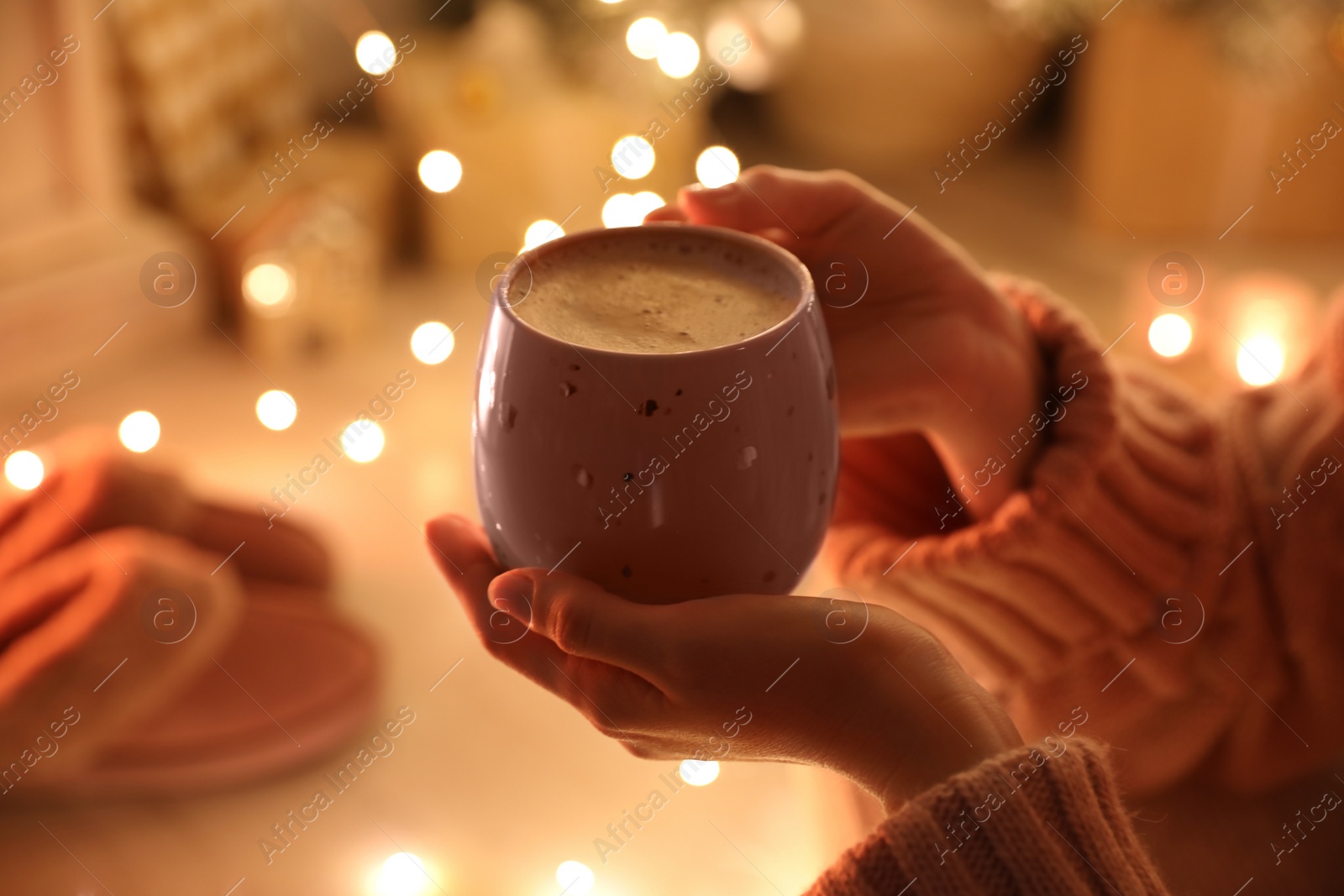 Photo of Woman with cup of drink and blurred Christmas lights on background, closeup