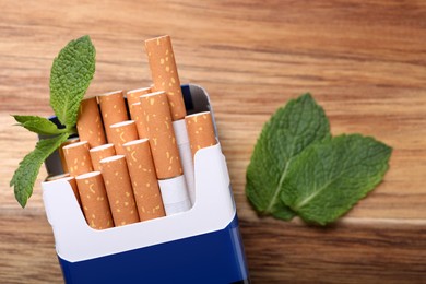 Photo of Pack of menthol cigarettes and mint leaves on wooden table, flat lay