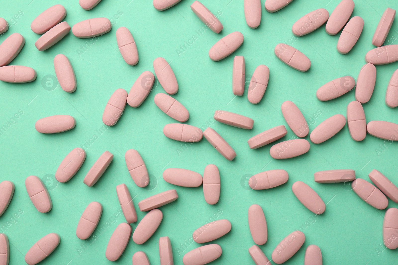 Photo of Pink vitamin capsules on turquoise background, top view
