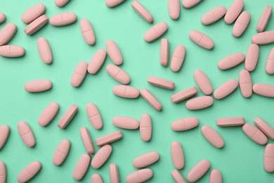 Photo of Pink vitamin capsules on turquoise background, top view