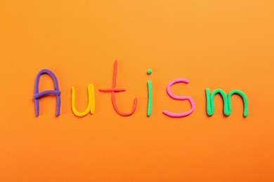 Photo of Word Autism made with colorful plasticine on orange background, flat lay