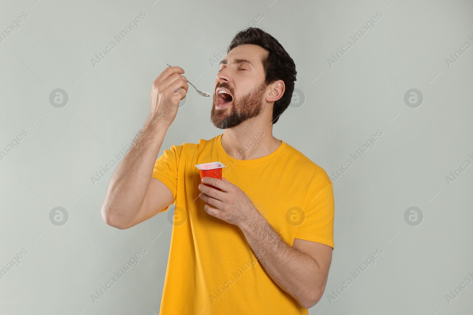 Photo of Handsome man eating delicious yogurt on light grey background