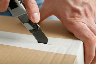 Man using utility knife to open parcel, closeup