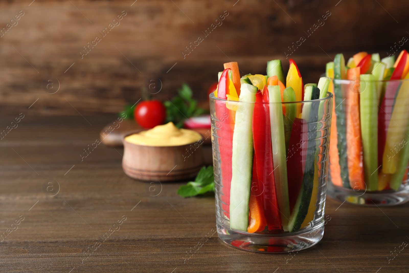 Photo of Fresh raw vegetable sticks in glasses on wooden table, space for text