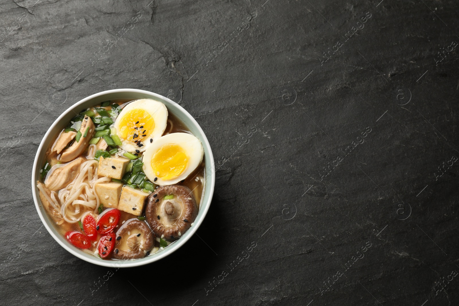 Photo of Noodle soup. Bowl of delicious ramen on black table, top view. Space for text