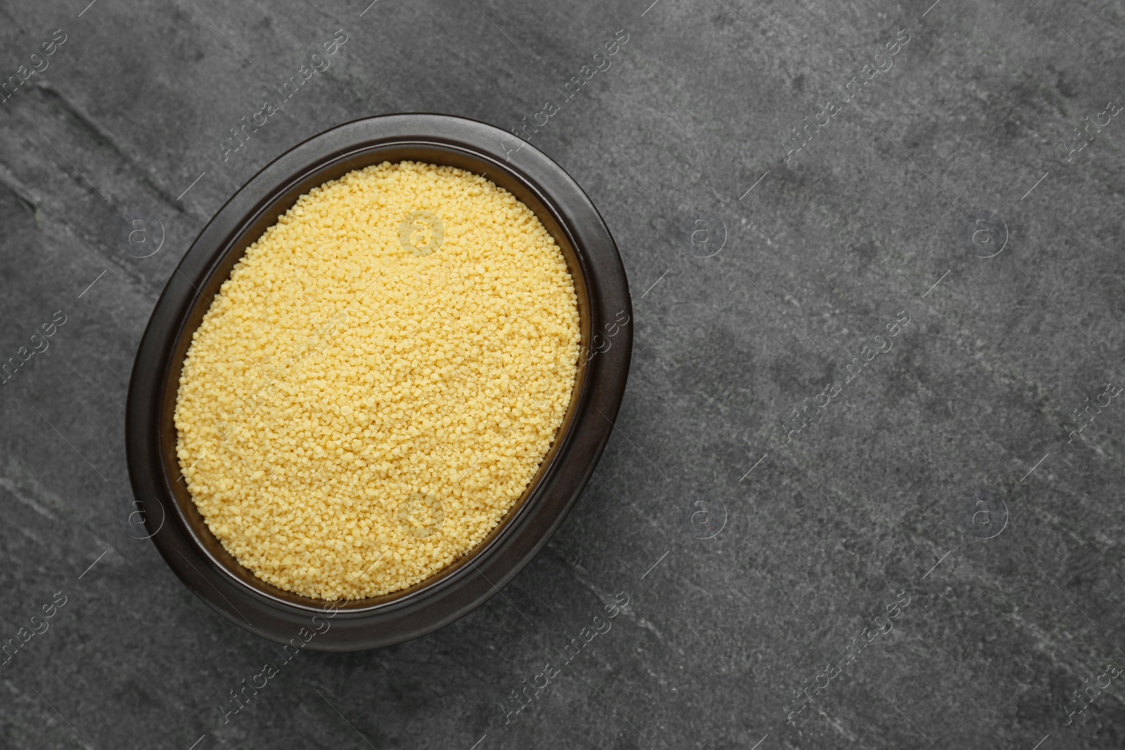 Photo of Bowl of raw couscous on grey table, top view. Space for text