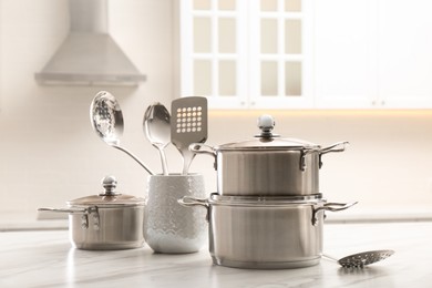 Photo of Set of stainless steel cookware and kitchen utensils on white table indoors