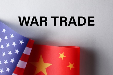 Photo of USA and China flags on paper with text WAR TRADE, flat lay