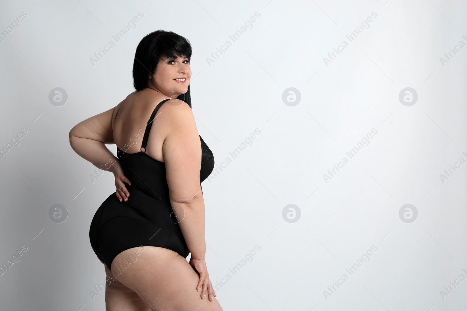 Photo of Beautiful overweight woman in black underwear on light background, space for text. Plus-size model