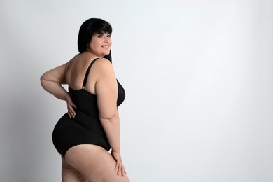 Photo of Beautiful overweight woman in black underwear on light background, space for text. Plus-size model