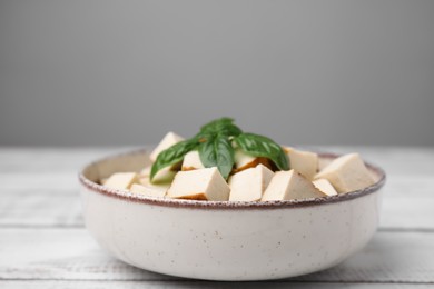 Photo of Bowl with delicious fried tofu and basil on white wooden table, closeup