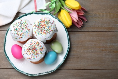 Photo of Easter cakes, painted eggs and tulips on wooden table, flat lay. Space for text