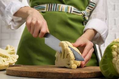 Photo of Woman cutting fresh cauliflower on wooden board, closeup
