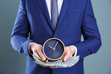Photo of Young businessman holding clock and money on color background. Time management