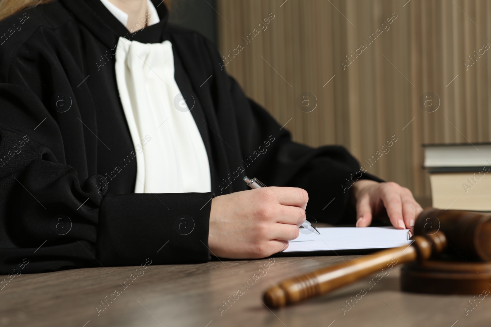 Photo of Judge with pen and clipboard working at wooden table in courtroom, closeup