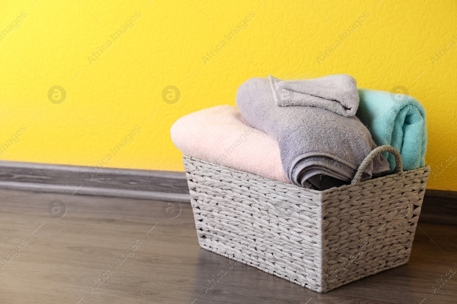 Photo of Basket with clean laundry on floor near yellow wall, space for text
