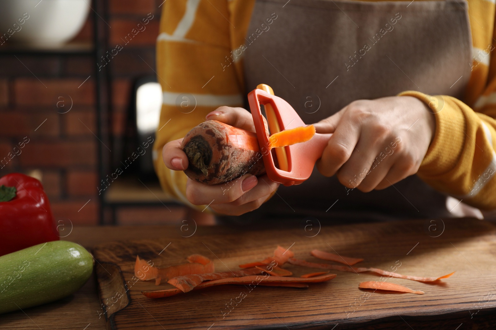 Photo of Woman peeling fresh carrot at table indoors, closeup