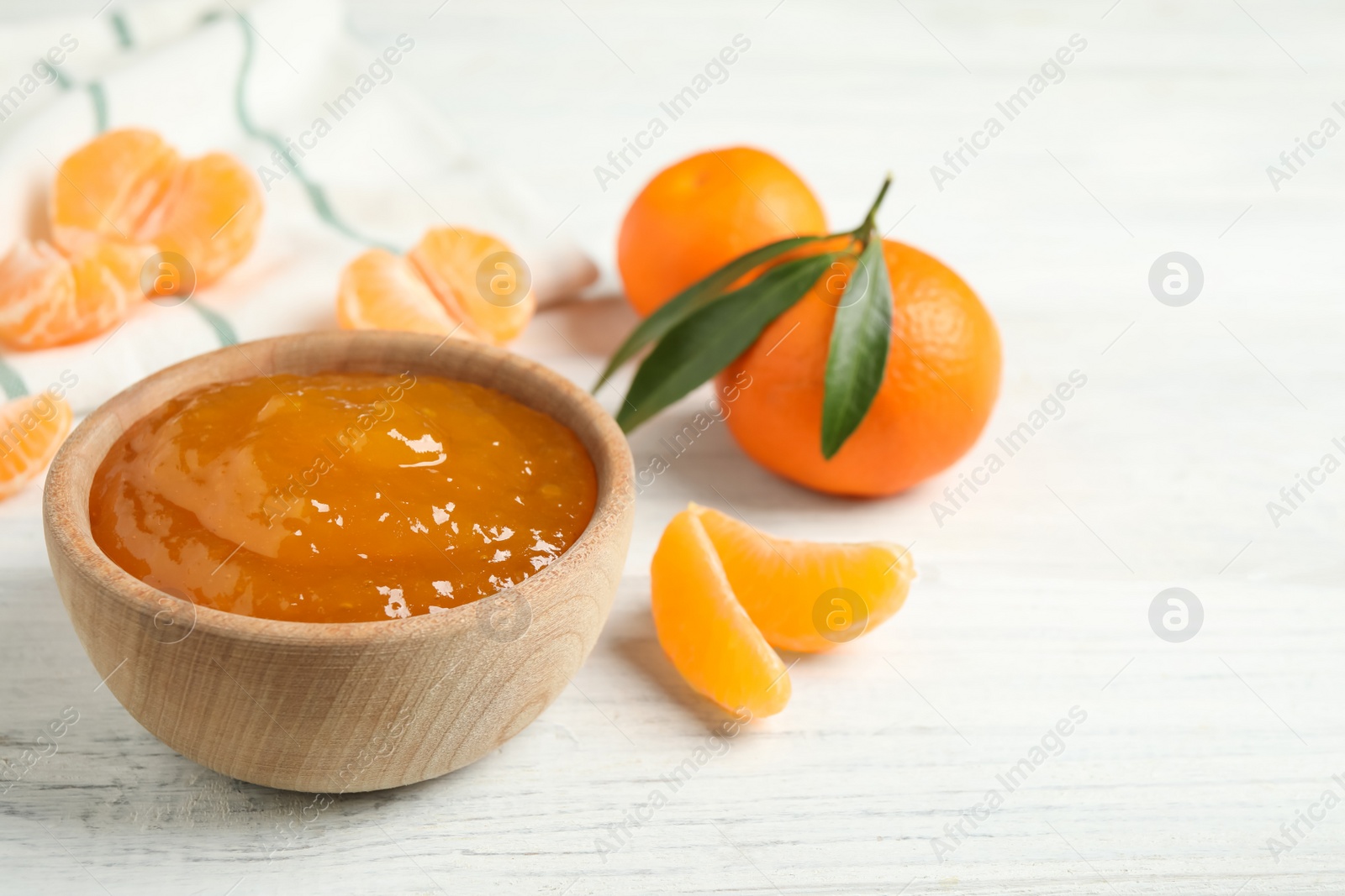 Photo of Tasty tangerine jam in wooden bowl on white table. Space for text