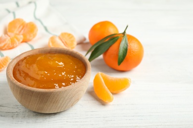 Tasty tangerine jam in wooden bowl on white table. Space for text