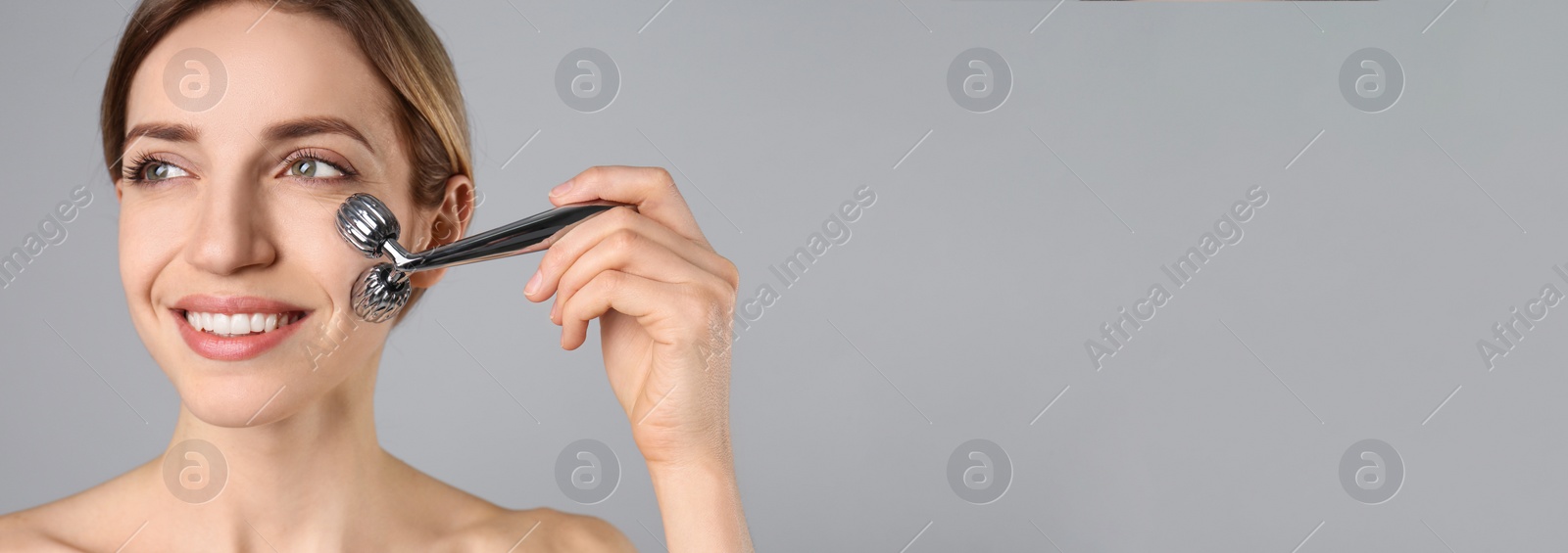 Image of Young woman using metal face roller on light grey background, space for text. Banner design