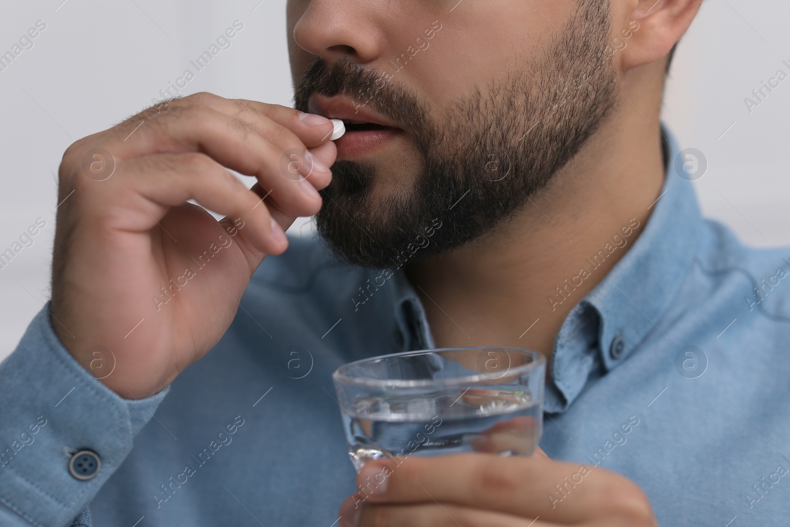 Photo of Man with glass of water taking antidepressant pill on light grey background, closeup
