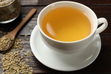 Photo of Fennel tea in cup and seeds on wooden table, closeup