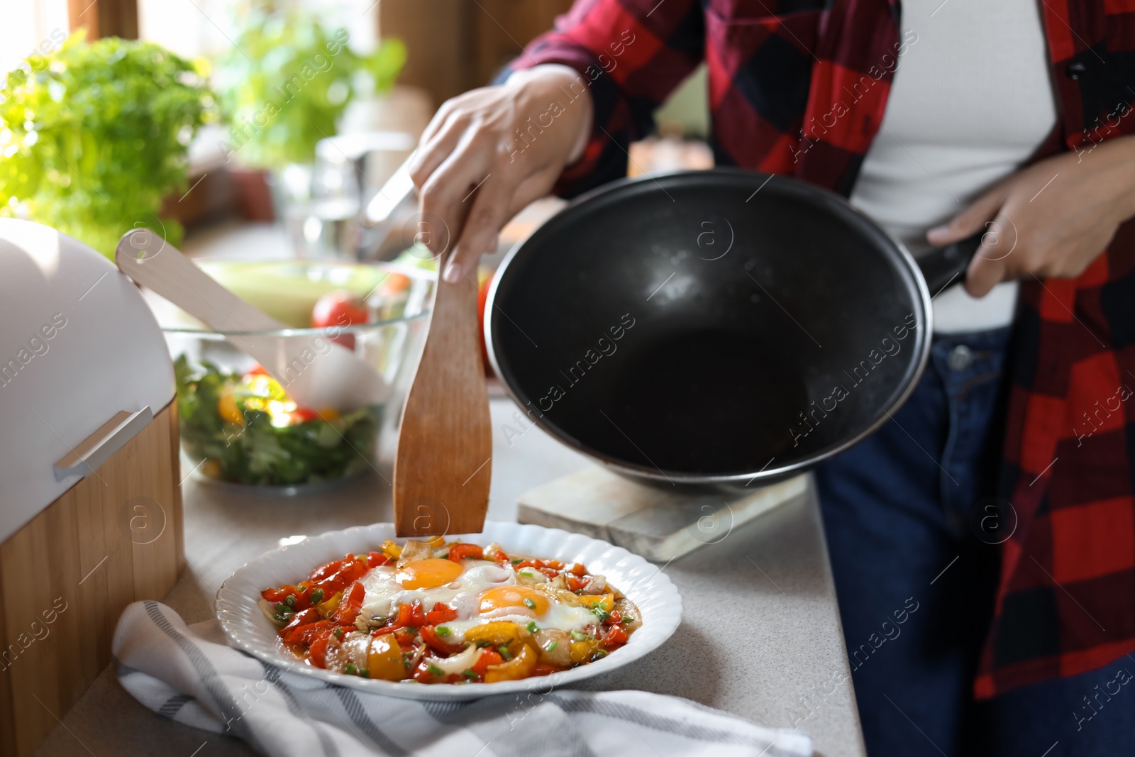 Photo of Woman putting freshly fried eggs with vegetables onto plate in kitchen, closeup