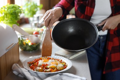 Woman putting freshly fried eggs with vegetables onto plate in kitchen, closeup