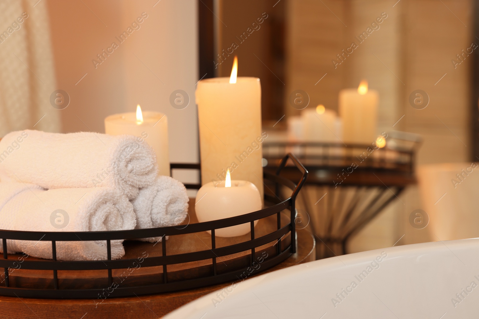 Photo of Rolled towels and burning candles on table near bath tub in bathroom