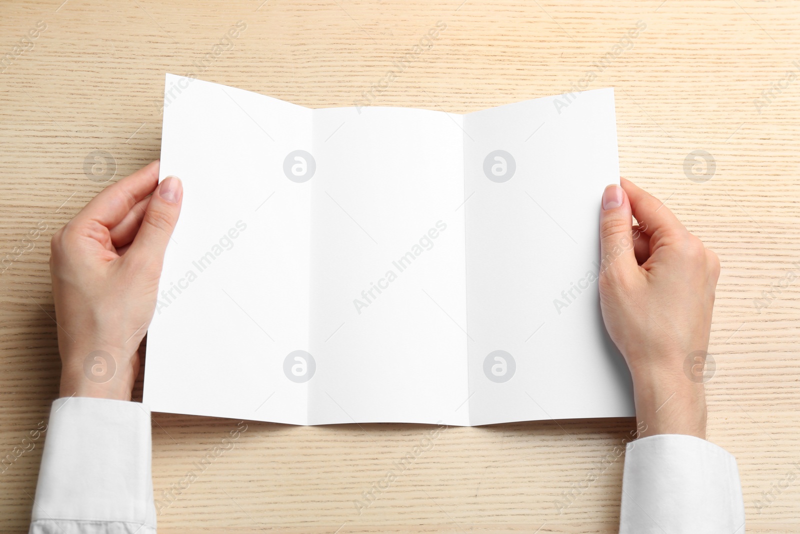 Photo of Young woman holding blank brochure at light wooden table, top view. Mock up for design