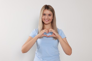 Happy volunteer making heart with her hands on light background