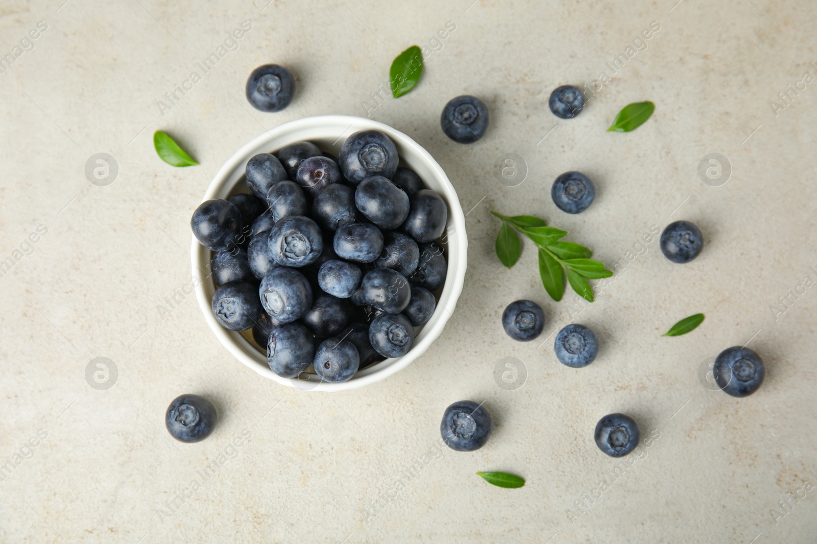 Photo of Bowl of tasty blueberries and leaves on light table, flat lay