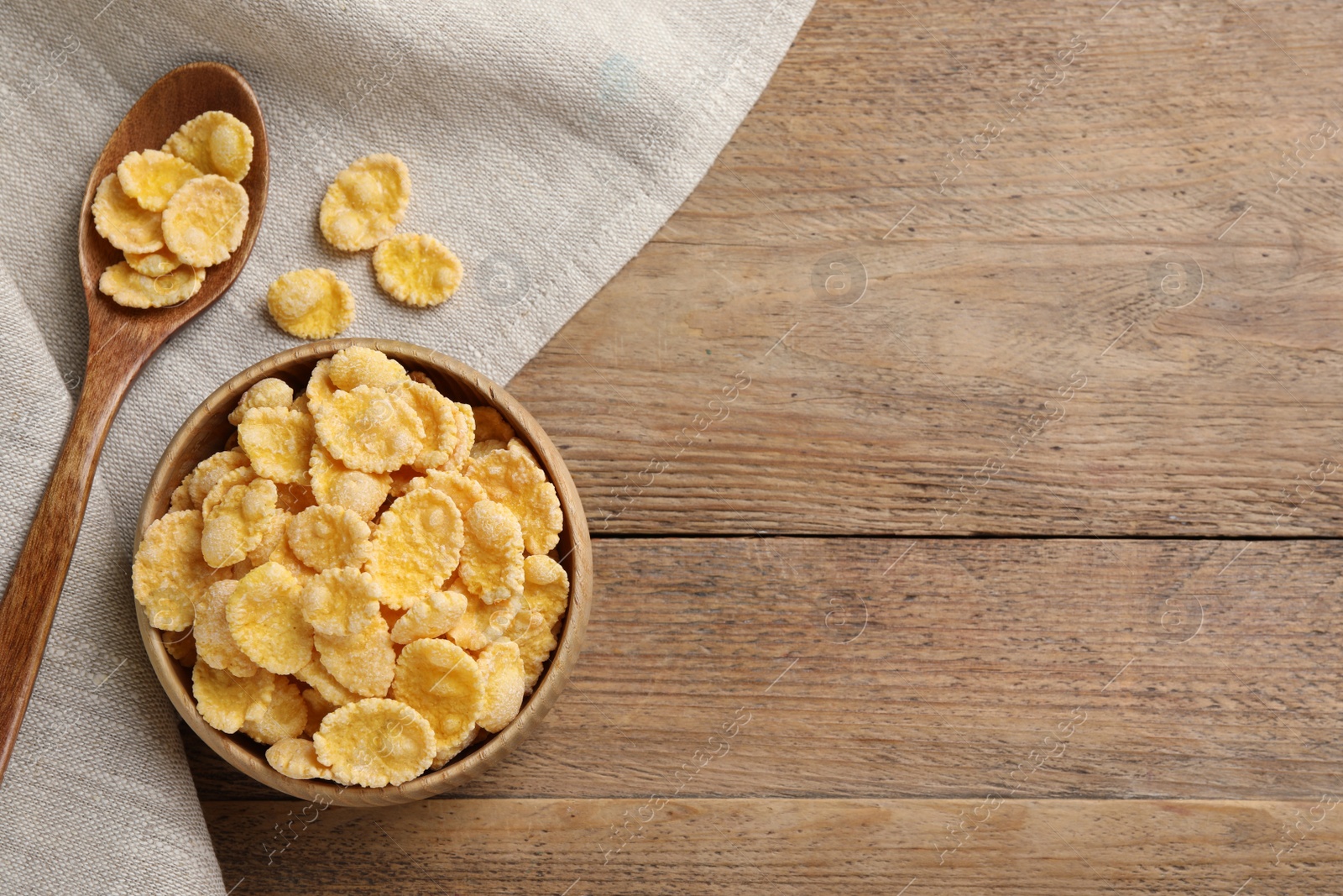 Photo of Bowl and spoon with tasty corn flakes on wooden table, top view. Space for text