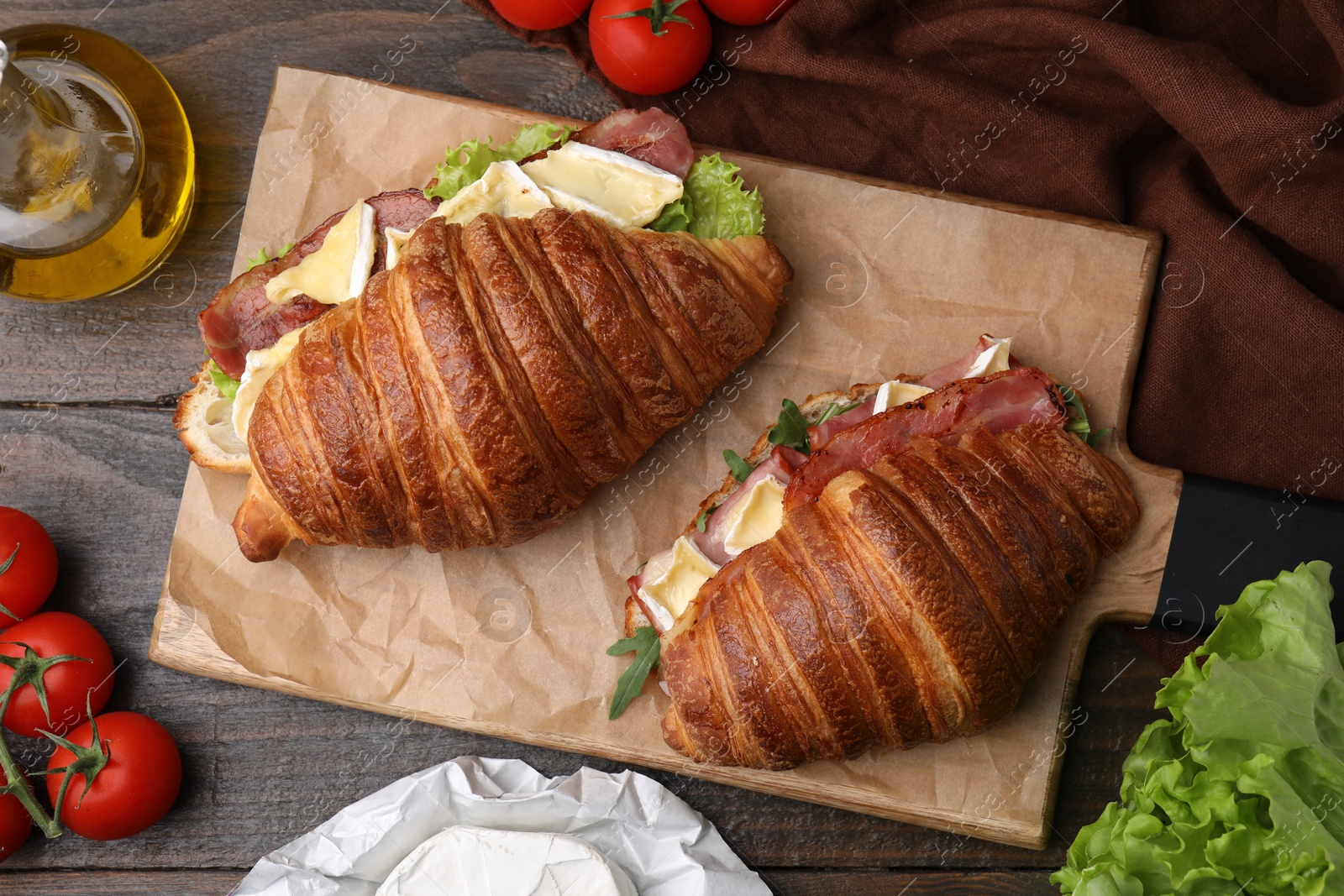 Photo of Tasty croissants with brie cheese, ham and bacon on wooden table, flat lay