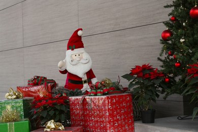 Photo of Funny Santa Claus, wrapped gifts and Christmas tree near building. Festive outdoor decoration