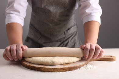 Photo of Man rolling dough with wooden pin at white table near grey wall, closeup