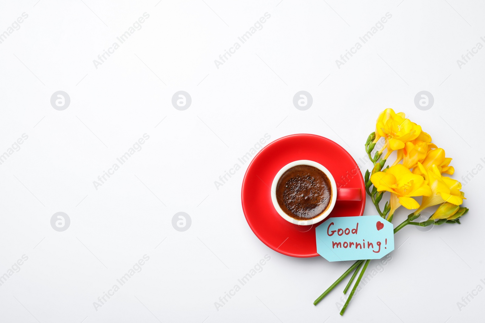 Photo of Cup of aromatic coffee, beautiful yellow freesias and Good Morning note on white background, flat lay. Space for text