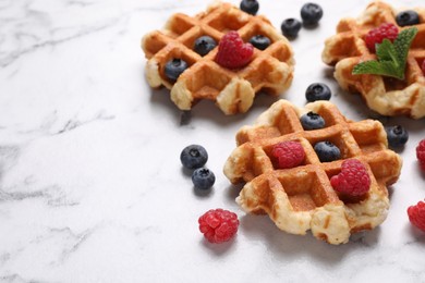 Photo of Delicious Belgian waffles with fresh berries and mint on white marble table, closeup. Space for text