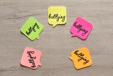 Photo of Stickers with word Bullying on wooden table, flat lay