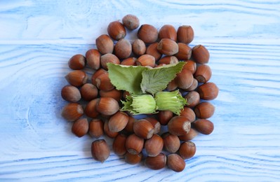 Photo of Pile of hazelnuts and leaves on light blue wooden table, flat lay